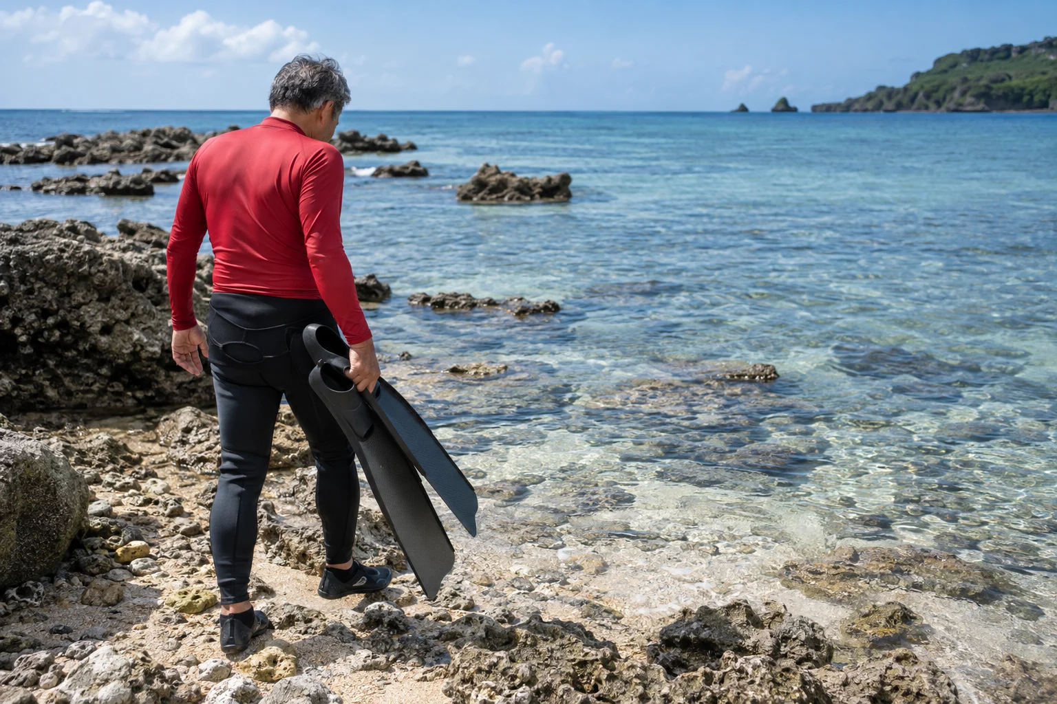 沖縄の海辺でロングフィンを持ち足元を確認する60代のスキンダイバー