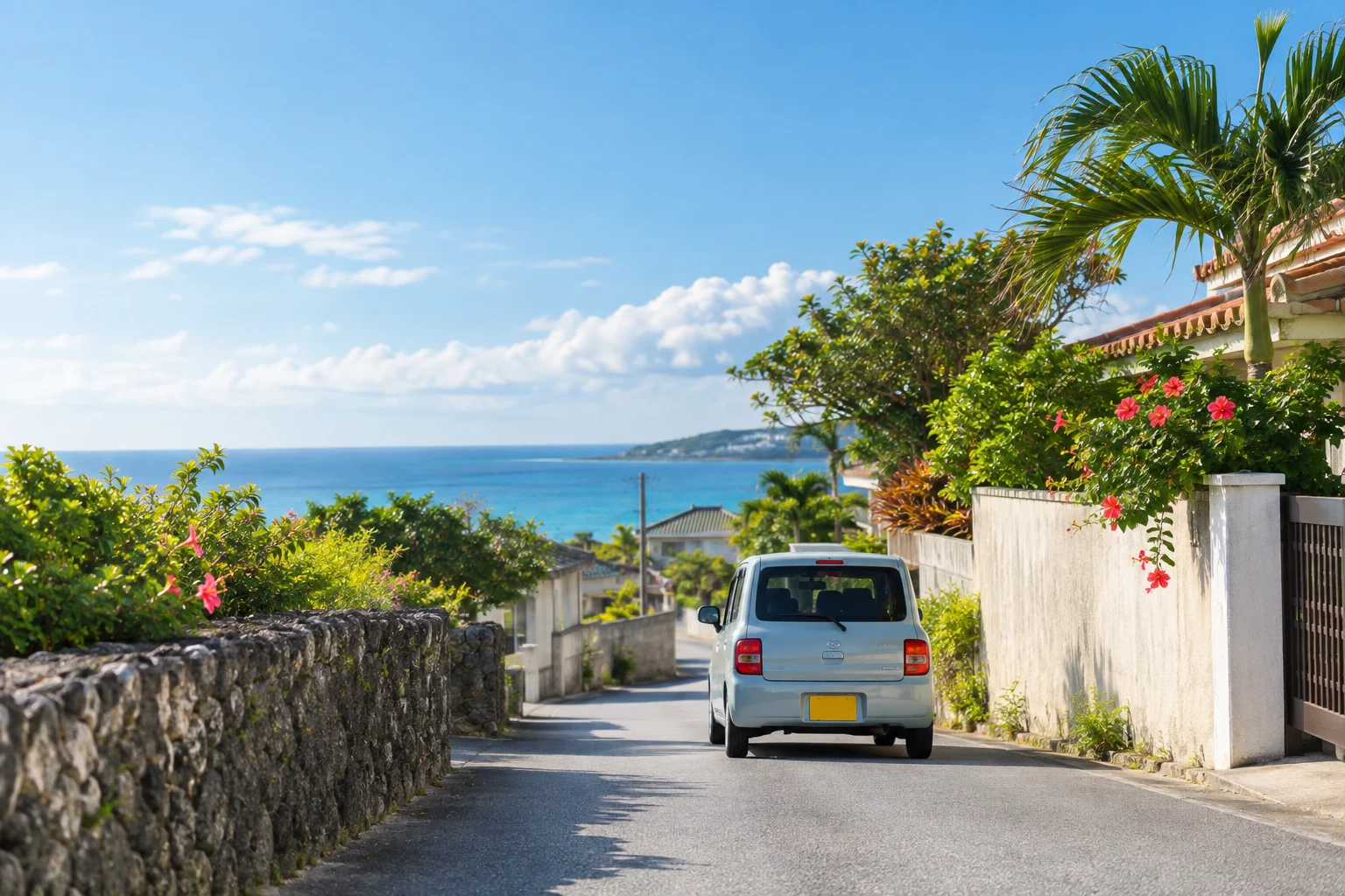 沖縄の住宅街の細い道を走る小さな車と、海へ向かう暮らしの風景
